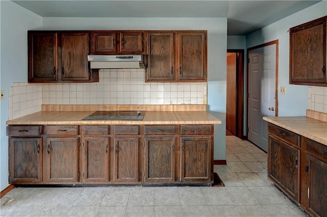 kitchen featuring under cabinet range hood, black electric cooktop, tasteful backsplash, and dark brown cabinets