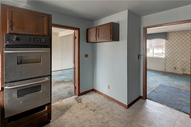 kitchen with dark brown cabinets, multiple ovens, wallpapered walls, baseboards, and light colored carpet