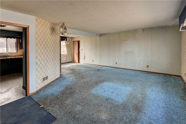 carpeted empty room with visible vents, a textured ceiling, baseboards, and a sink