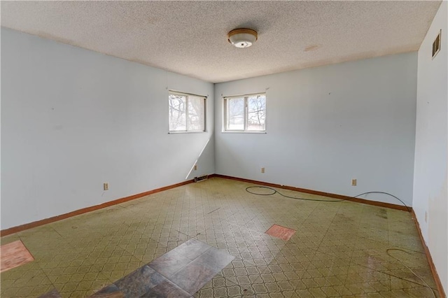 unfurnished room featuring tile patterned floors, visible vents, a textured ceiling, and baseboards