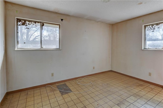 unfurnished room with a healthy amount of sunlight, baseboards, light floors, and a textured ceiling