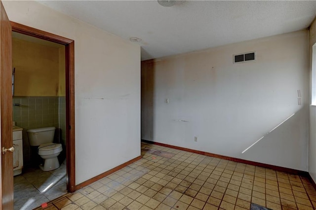 spare room featuring tile walls and visible vents