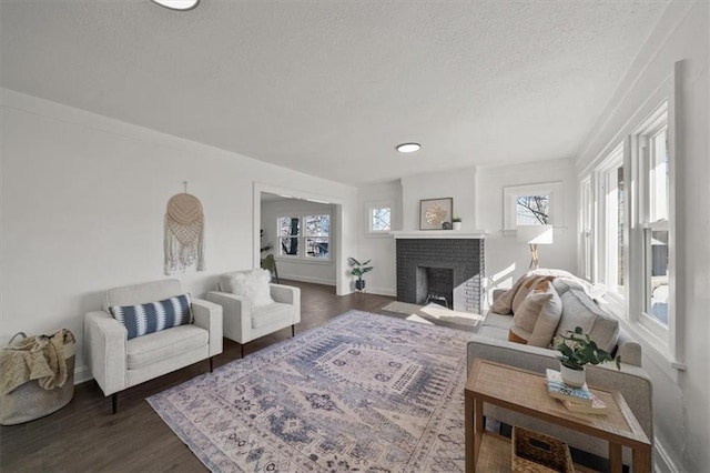 living room with dark wood finished floors, a brick fireplace, a textured ceiling, and baseboards