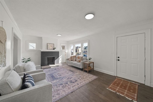 living area featuring a brick fireplace, a textured ceiling, baseboards, and wood finished floors