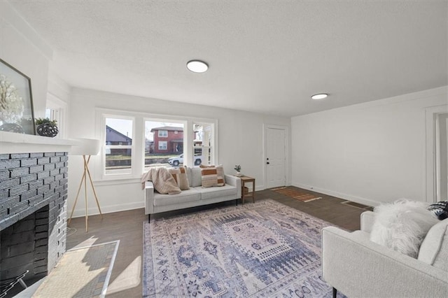 living room featuring baseboards, a textured ceiling, a brick fireplace, and wood finished floors