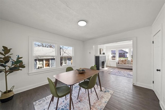 dining room with baseboards, a textured ceiling, a brick fireplace, and wood finished floors