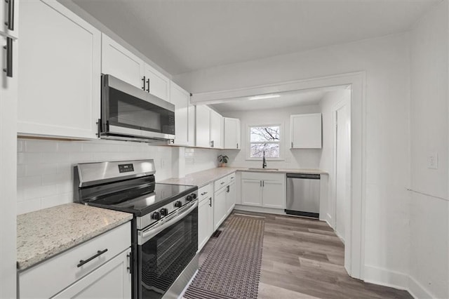 kitchen featuring wood finished floors, a sink, decorative backsplash, stainless steel appliances, and white cabinets