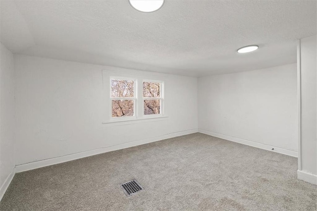 carpeted spare room with visible vents, baseboards, and a textured ceiling