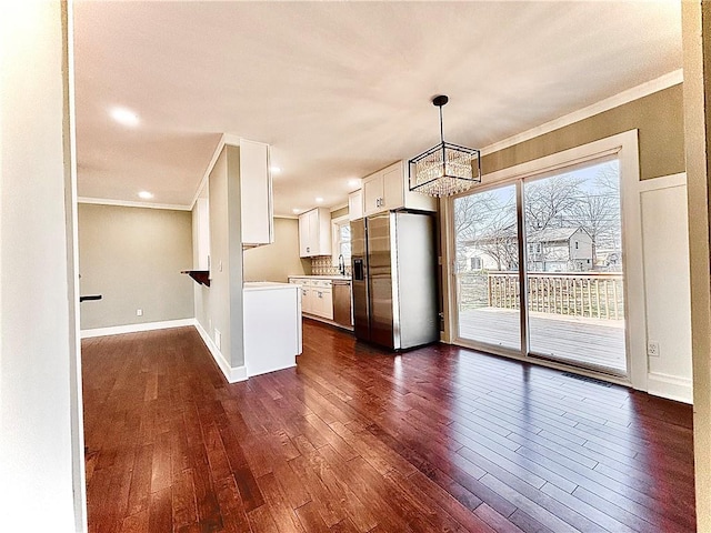 kitchen with dark wood-type flooring, crown molding, appliances with stainless steel finishes, an inviting chandelier, and white cabinets