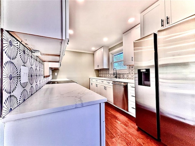 kitchen with light stone counters, decorative backsplash, stainless steel appliances, wood finished floors, and white cabinetry