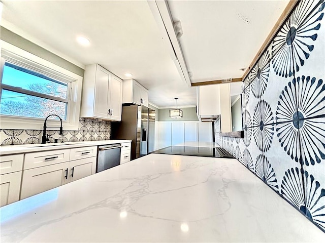 kitchen with light stone countertops, a sink, decorative backsplash, appliances with stainless steel finishes, and white cabinetry