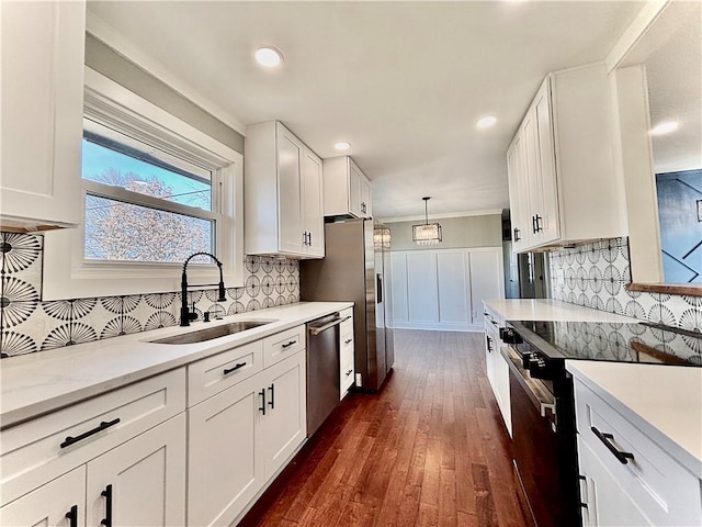 kitchen with stainless steel appliances, a sink, dark wood-type flooring, white cabinets, and pendant lighting