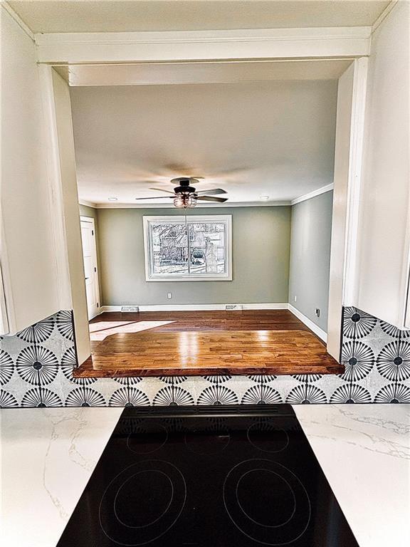 interior space with wood finished floors, stovetop, crown molding, light stone countertops, and ceiling fan