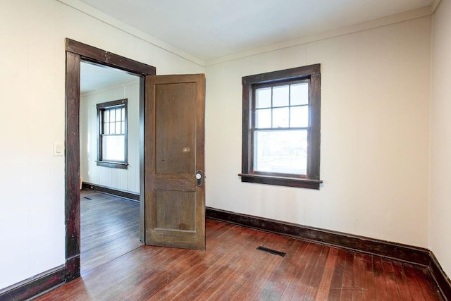 spare room with hardwood / wood-style flooring, crown molding, visible vents, and baseboards