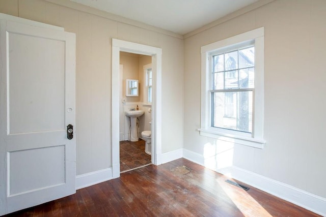 unfurnished bedroom featuring visible vents, a sink, wood finished floors, a decorative wall, and baseboards