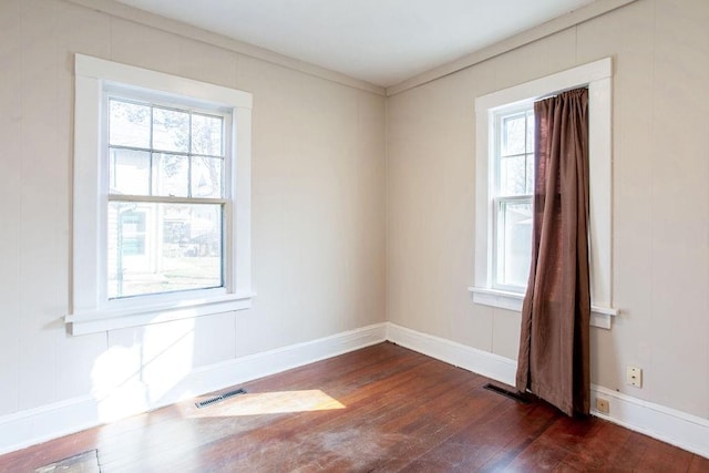 empty room with visible vents, a healthy amount of sunlight, dark wood-type flooring, and baseboards