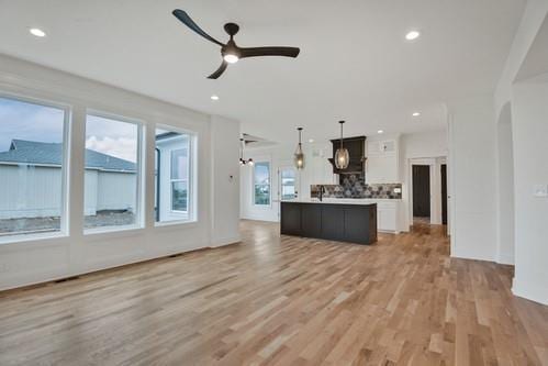 unfurnished living room featuring light wood-style flooring, arched walkways, a ceiling fan, and recessed lighting