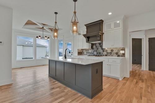 kitchen featuring white cabinets, light countertops, light wood finished floors, a center island with sink, and backsplash