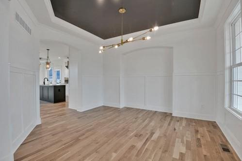 unfurnished dining area with a decorative wall, visible vents, a tray ceiling, and wainscoting