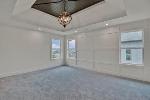 carpeted empty room with baseboards, a raised ceiling, an inviting chandelier, a decorative wall, and recessed lighting