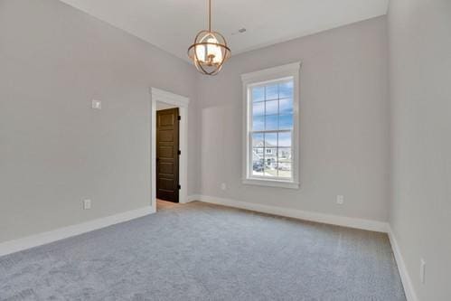 spare room featuring a chandelier, carpet flooring, and baseboards
