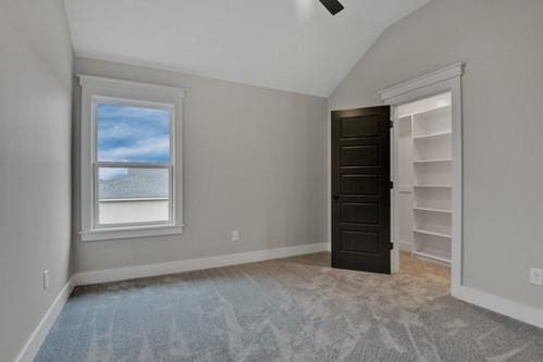 unfurnished bedroom with baseboards, a walk in closet, carpet flooring, and lofted ceiling