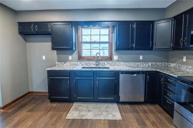 kitchen featuring light stone counters, baseboards, dark wood-style flooring, a sink, and stainless steel appliances