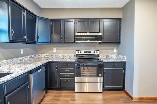 kitchen featuring light stone counters, ventilation hood, appliances with stainless steel finishes, light wood finished floors, and baseboards