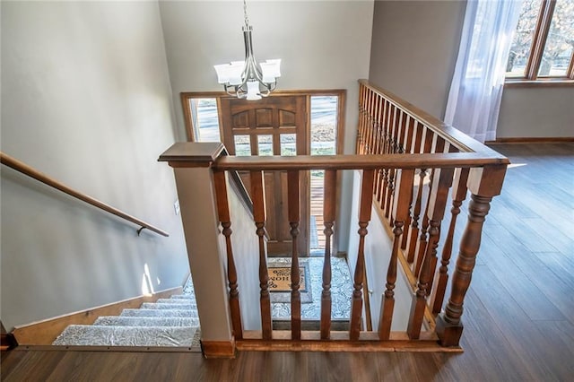 staircase with a notable chandelier, a towering ceiling, baseboards, and wood finished floors