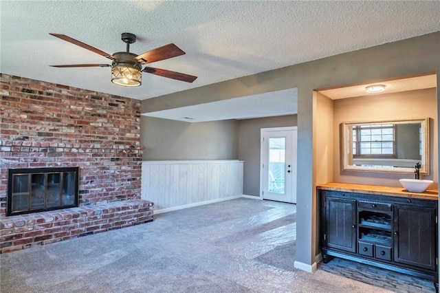 unfurnished living room with carpet flooring, a textured ceiling, ceiling fan, and a sink