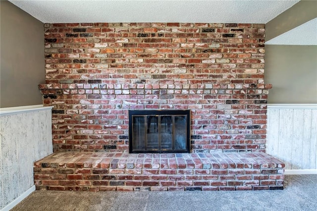 details with a textured ceiling, wood walls, carpet flooring, a fireplace, and wainscoting