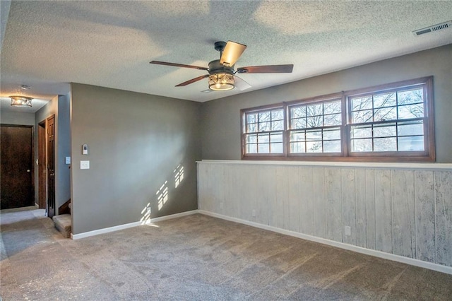 carpeted empty room with visible vents, plenty of natural light, a textured ceiling, and a ceiling fan