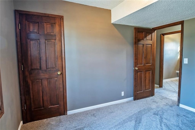 unfurnished room with a textured ceiling, baseboards, and light carpet