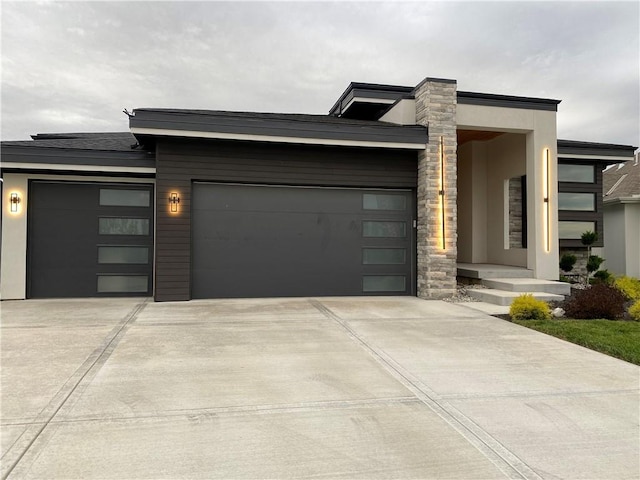 contemporary home with concrete driveway, an attached garage, stone siding, and stucco siding