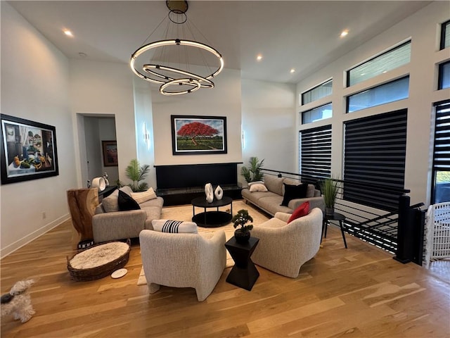 living room featuring wood finished floors, baseboards, recessed lighting, a towering ceiling, and a notable chandelier