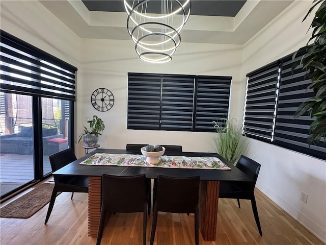 dining area featuring a tray ceiling, baseboards, an inviting chandelier, and wood finished floors