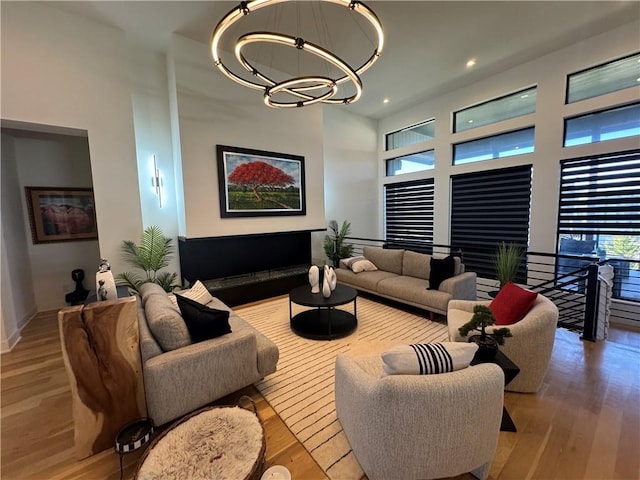 living area with recessed lighting, a notable chandelier, wood finished floors, and a towering ceiling