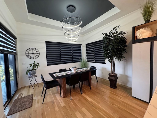 dining space with a tray ceiling, a notable chandelier, visible vents, and wood finished floors