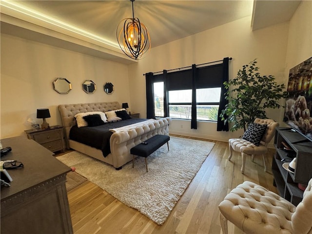 bedroom with a tray ceiling, light wood-style floors, and an inviting chandelier