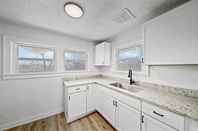 kitchen featuring visible vents, light wood-type flooring, light stone counters, white cabinetry, and a sink