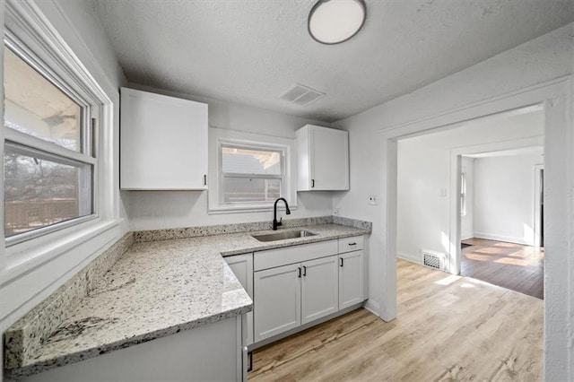 kitchen featuring white cabinets, light wood-type flooring, visible vents, and a sink