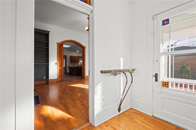 entryway with baseboards, light wood-type flooring, arched walkways, and visible vents