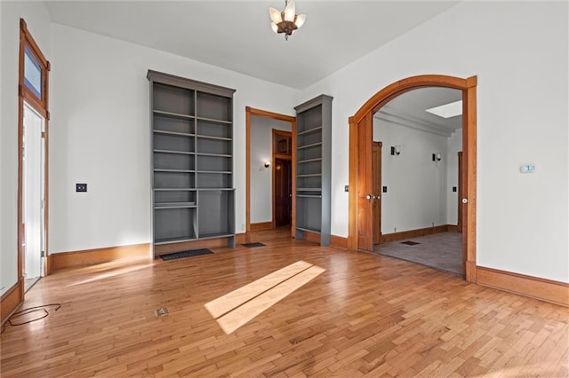 empty room featuring arched walkways, light wood-style flooring, and baseboards