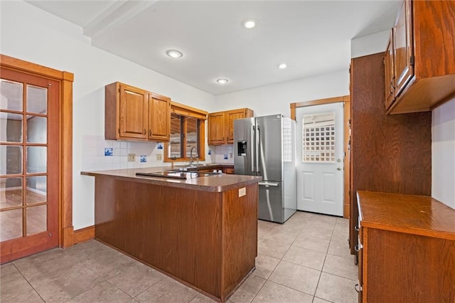 kitchen with tasteful backsplash, a peninsula, stainless steel refrigerator with ice dispenser, light tile patterned flooring, and brown cabinetry