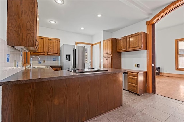 kitchen with dark countertops, stainless steel fridge with ice dispenser, a peninsula, black electric cooktop, and a sink