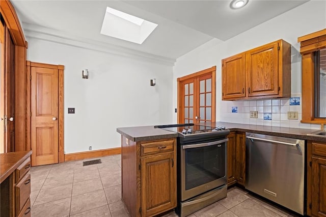 kitchen featuring a peninsula, a skylight, dark countertops, and stainless steel appliances