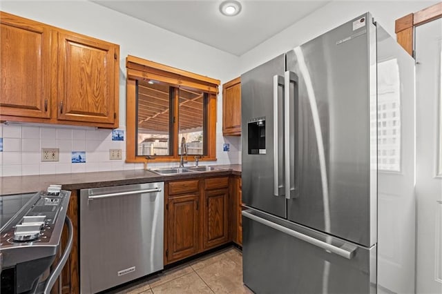 kitchen with light tile patterned floors, stainless steel appliances, dark countertops, brown cabinets, and backsplash