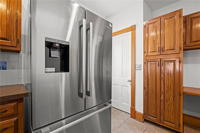 kitchen with dark countertops, stainless steel fridge with ice dispenser, light tile patterned floors, decorative backsplash, and brown cabinets