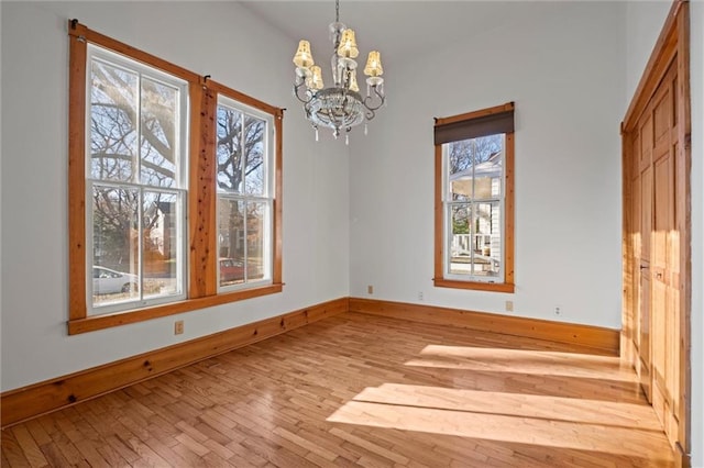 unfurnished dining area with hardwood / wood-style floors, baseboards, a healthy amount of sunlight, and a chandelier