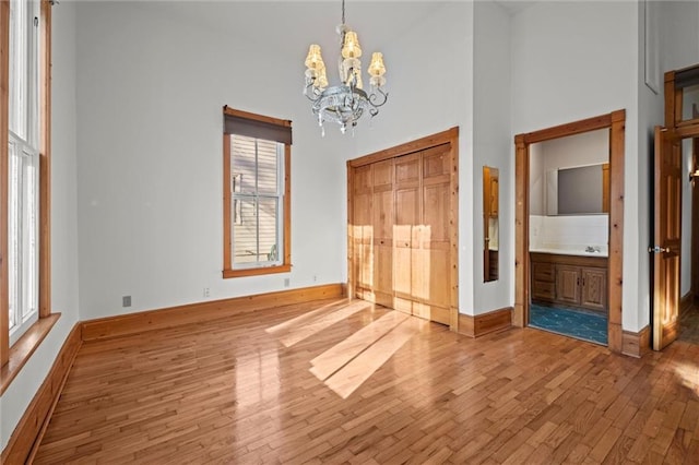 unfurnished bedroom with an inviting chandelier, light wood-style floors, baseboards, and a towering ceiling